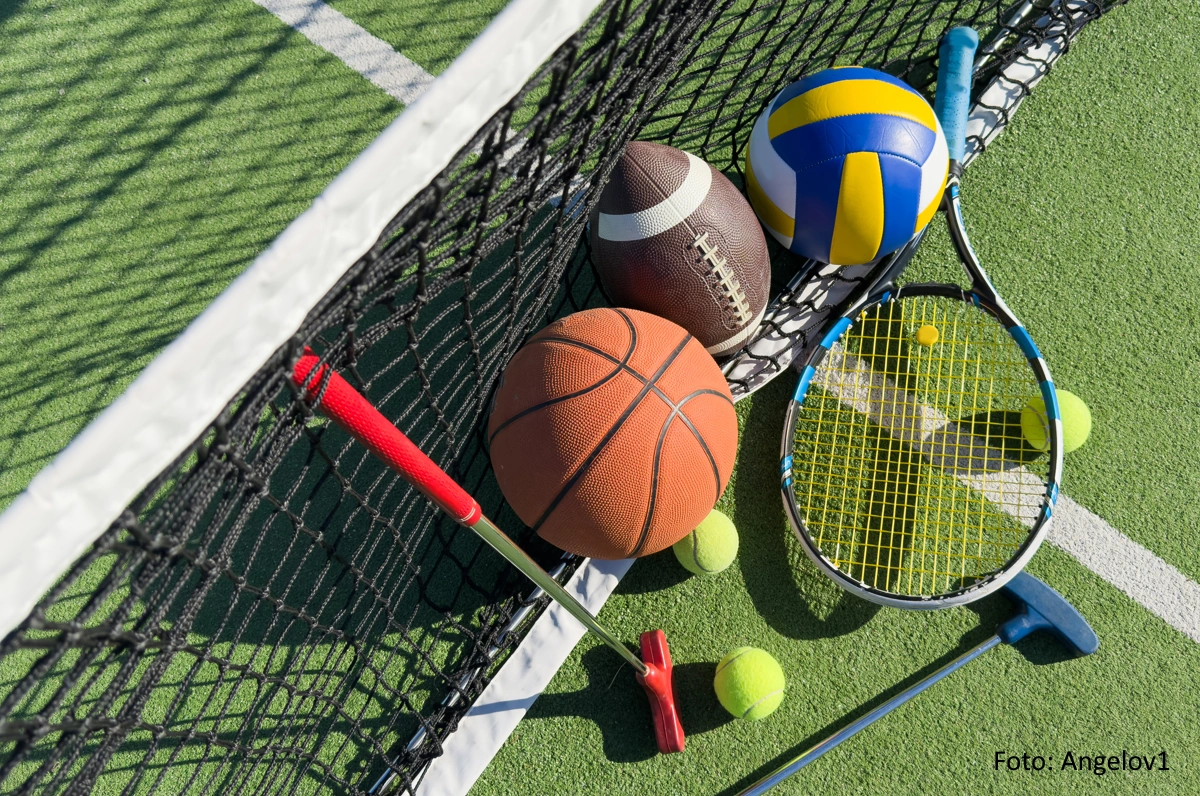 Diverse Bälle und Schläger unterschiedlicher Sportarten liegen am Netz eines Tennisplatzes