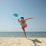 Mann hechtet am Strand und bei sonnigem Wetter auf eine Frisbee zu