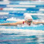 Nachwuchsschwimmerin mit weißer Kappe im Schmetterlingsstil auf einer Wettkampfbahn
