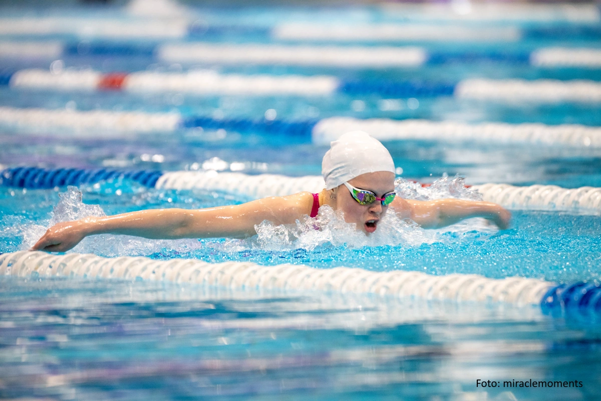 Nachwuchsschwimmerin mit weißer Kappe im Schmetterlingsstil auf einer Wettkampfbahn