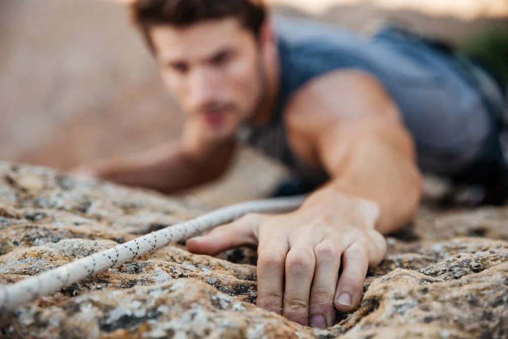Man reaching for a grip while he rock climbs on a steep cliff