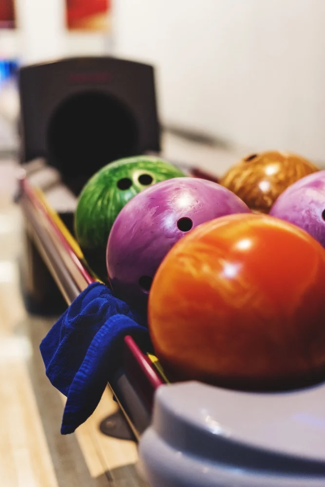 Bunte Bowlingbälle liegen aufgereiht auf der Kugelablage