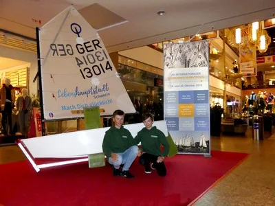 Ist nach 30 Jahren auch in der Schweriner Innenstadt angekommen und macht Werbung für den Segelsport an Land: Der Opti, stolz präsentiert von den Schweriner Seglern Reamon und Noel Theiner im Schlossparkcenter. Bild: © Veranstalter Ist nach 30 Jahren auch in der Schweriner Innenstadt angekommen und macht Werbung für den Segelsport an Land: Der Opti, stolz präsentiert von den Schweriner Seglern Reamon und Noel Theiner im Schlossparkcenter (© Veranstalter).