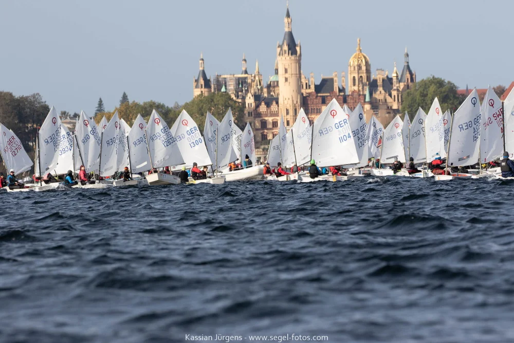 Ein Bild aus vergangenen, unbeschwerten Zeiten: Die Segler der Bootsklasse Optimist vor der Kulisse des Schweriner Schlosses beim Herbstpokal 2019 © Kassian Jürgens www.segel-fotos.com