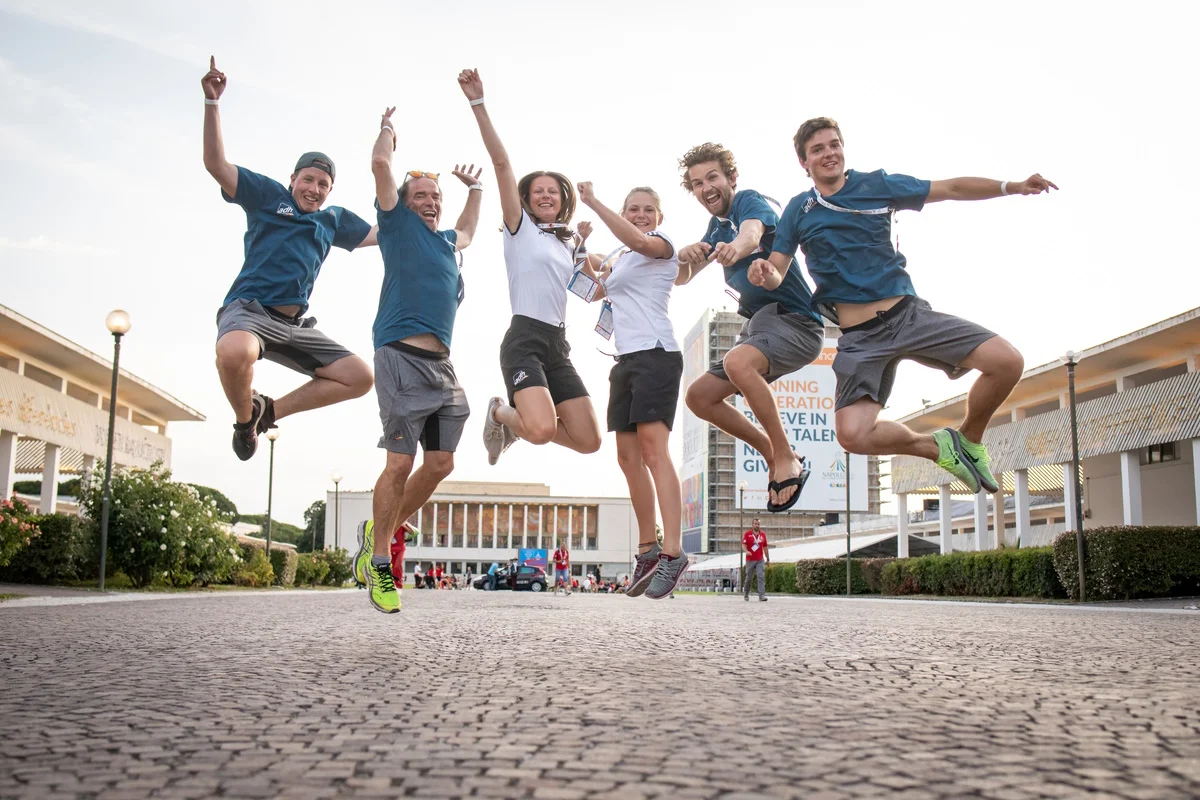 6 deutsche Sportler:innen springen freudig in die Luft. Im Hintergrund: das Stadion San Paolo. Foto: © Arndt Falter
