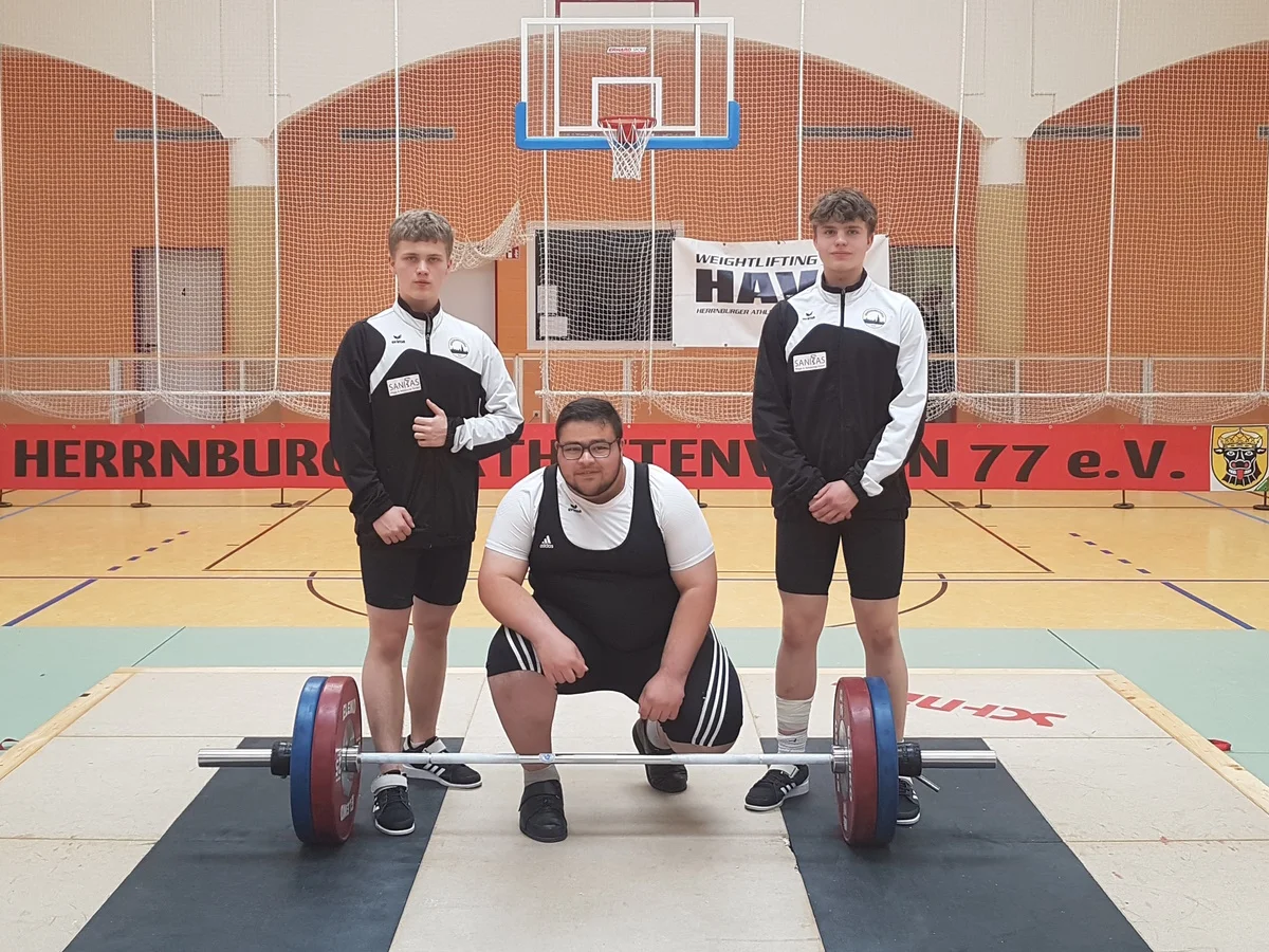 Gewichthebertrio posiert hinter einer Langhantel