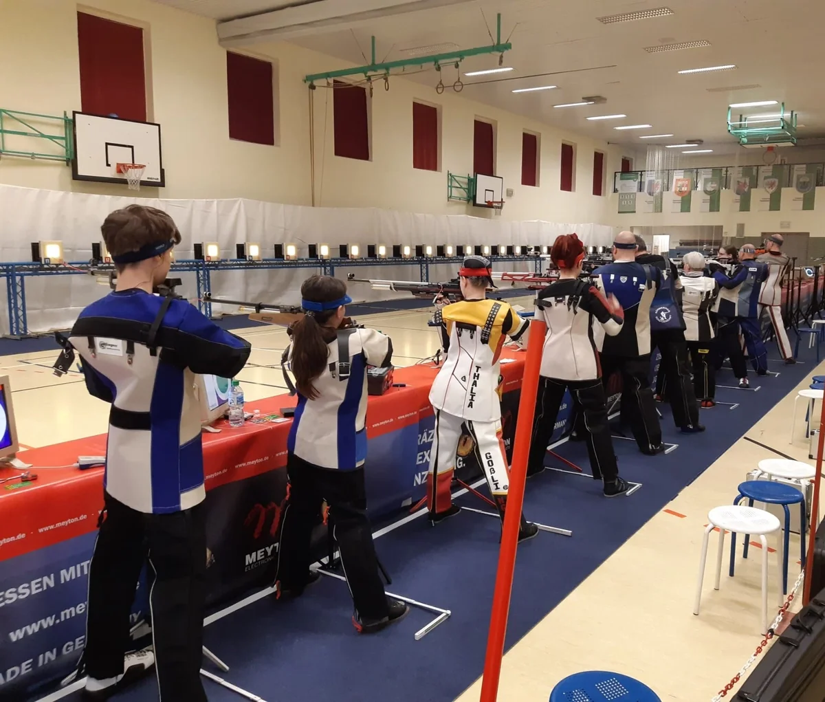 10 Junge und ältere Sportschütz:innen beim Anvisieren der Zielscheibe. Für die Landesmeisterschaft MV wurde eigens eine Sporthalle zum Schießplatz hergerichtet.