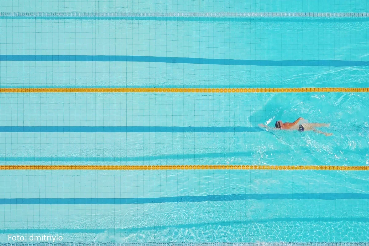 Schwimmbecken von oben. ein einzelner Schwimmer zieht seine Bahnen.