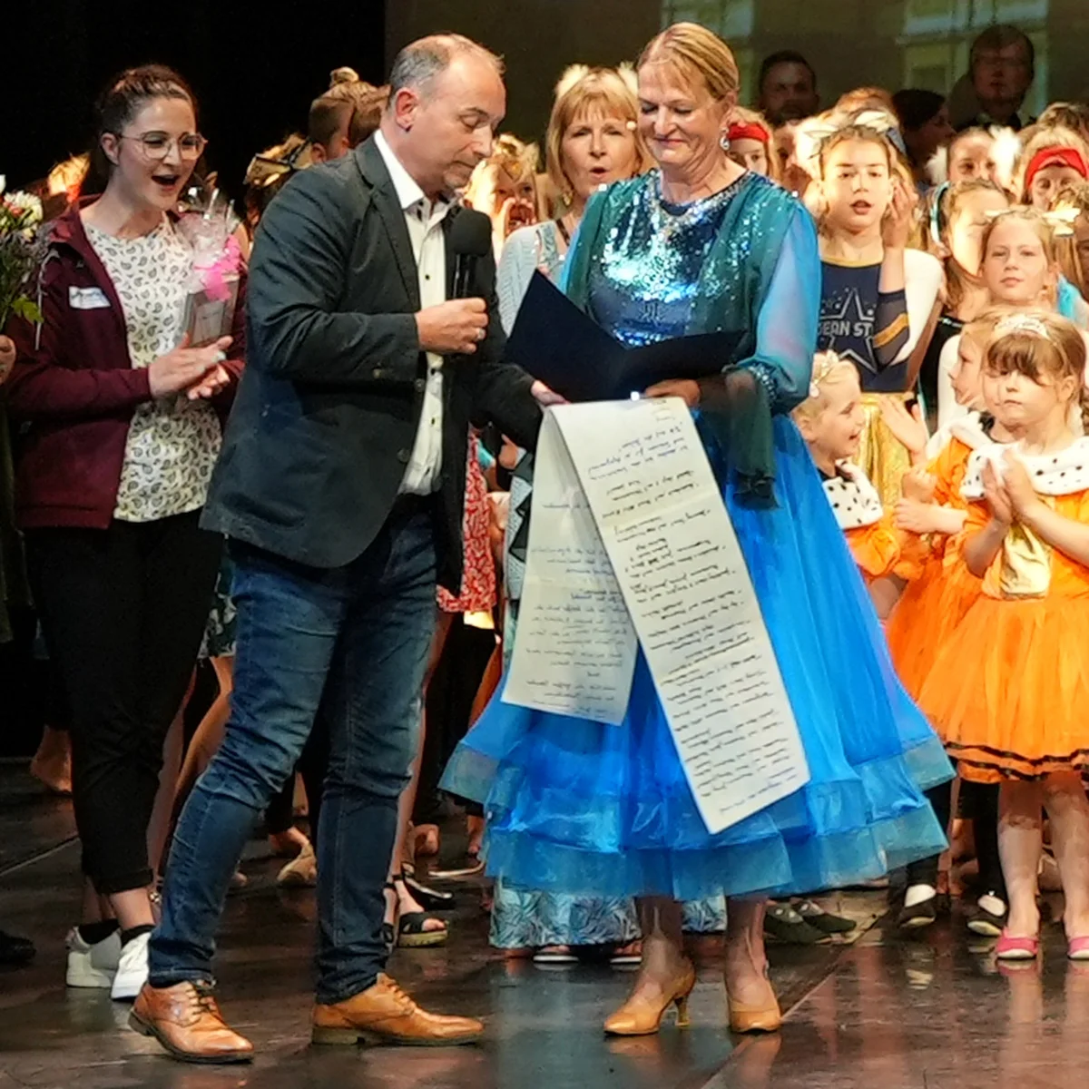 Astrid Rose in langem blauen Tanzkleid wird in Anwesenheit ihrer Tänzerinnen geehrt.