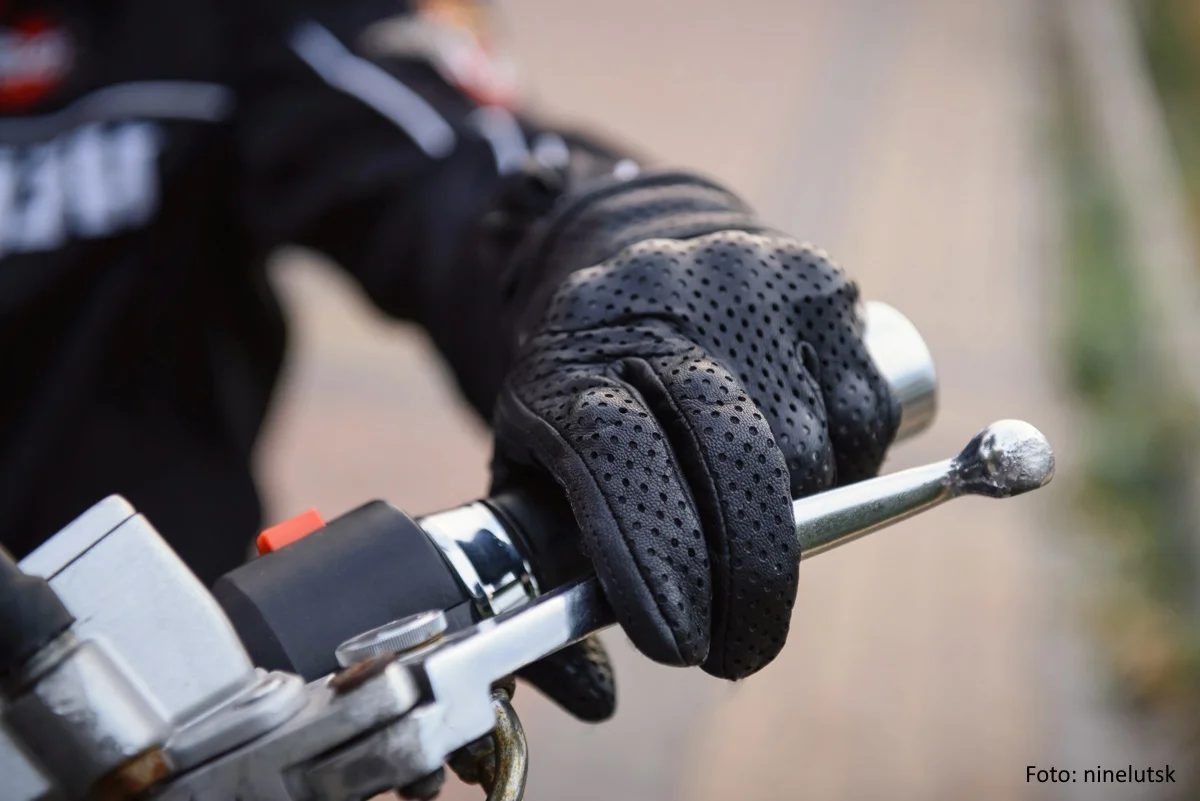 Hand eines Motorradfahres mit schwarzem Handschuh am Lenker