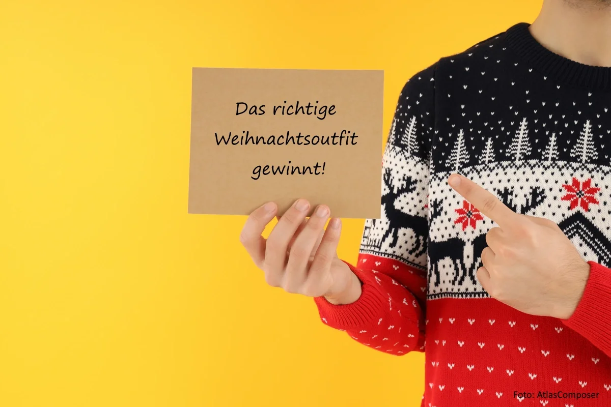Mann in gestricktem Weihnachtspulli (vor gelbem Hintergrund) zeigt auf eine beschriftete Karte.