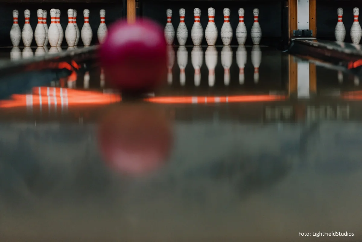 roter Bowlingball rollt auf der Bahn auf die aufgestellten Pins zu