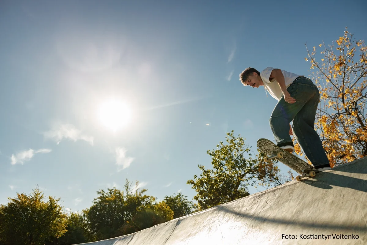 Skateboarder steht bei strahlendem Sonnenschein auf der Kante einer Halfpipe.
