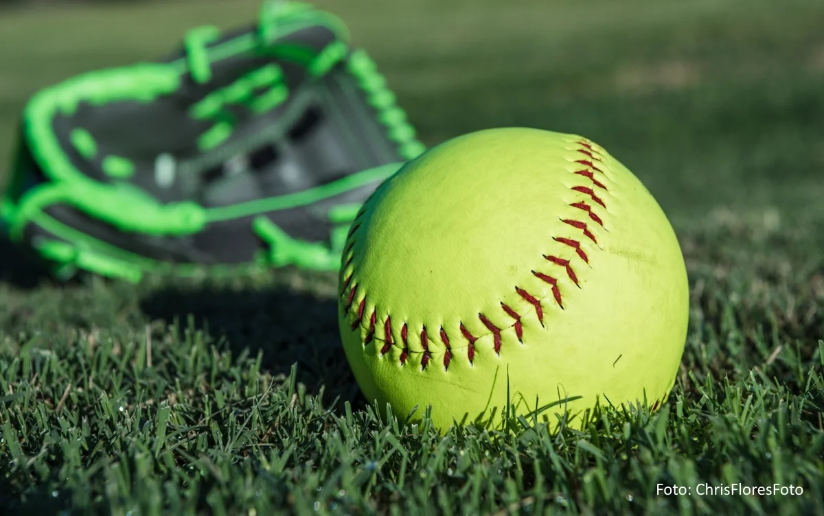 Gelber Softball samt grün-schwarzer Handschuh auf einer Rasenfläche