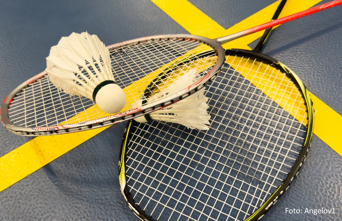 Zwei Badmintonschläger und Federbälle liegen auf einem blauen Court mit gelben Linien