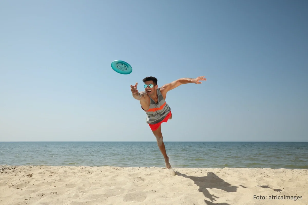 Mann hechtet am Strand und bei sonnigem Wetter auf eine Frisbee zu