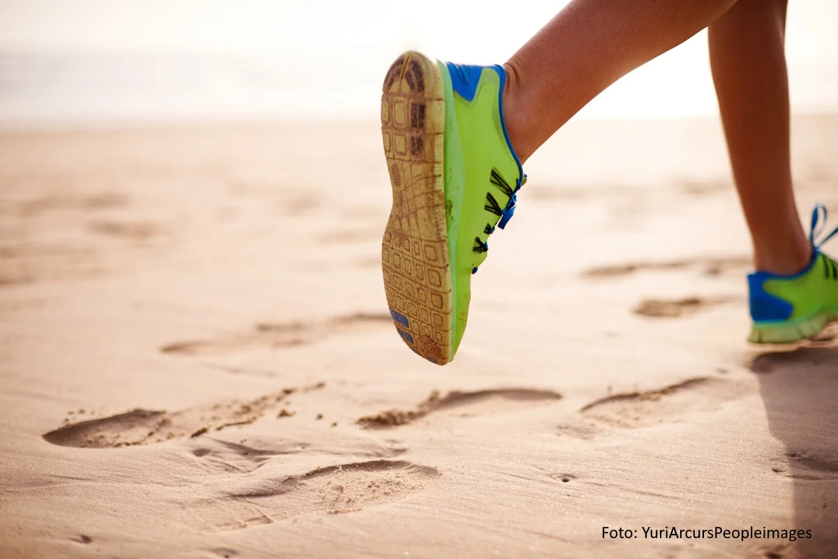 Läufer:in in grünen Sportschuhen am Sandstrand. Blick auf die Schuhe und Unterschenkel.