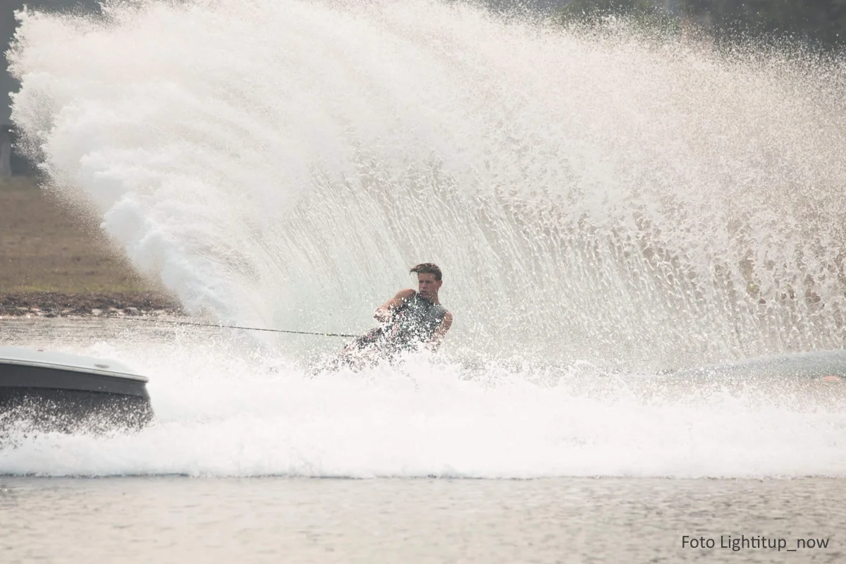 Männlicher Jugendlicher auf einem Wakeboard erzeugt bei einer Wende riesige Wasserspritzer