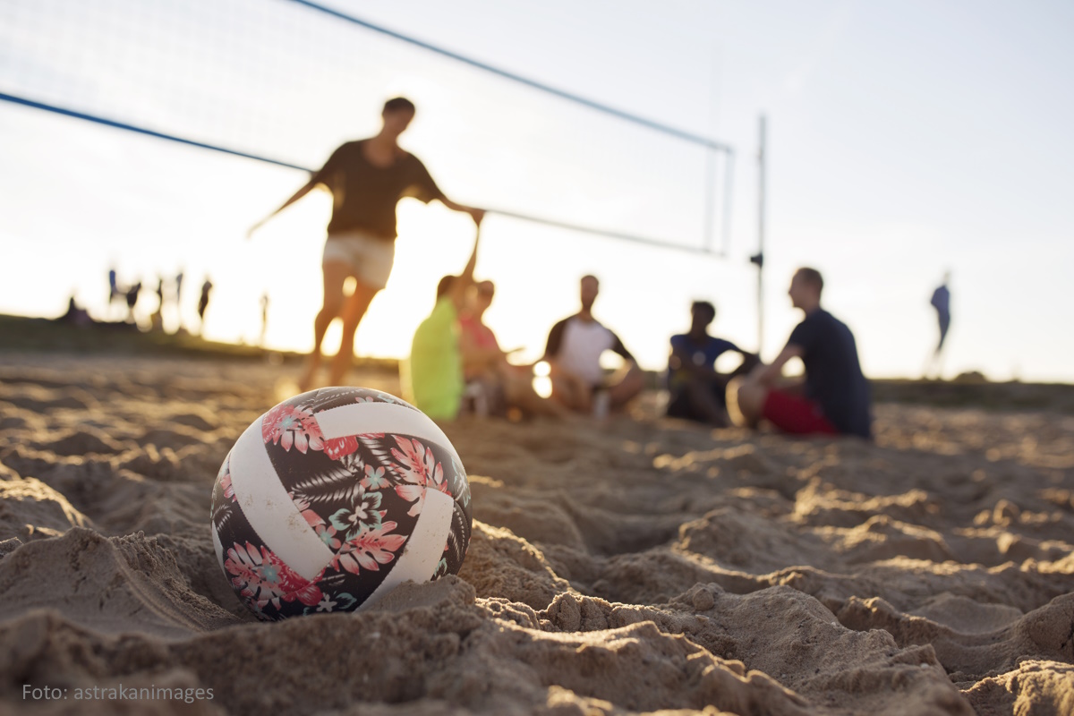 Gruppe von Menschen sitzen nach dem Beachvolleyball spielen in der Abendsonne im Sand