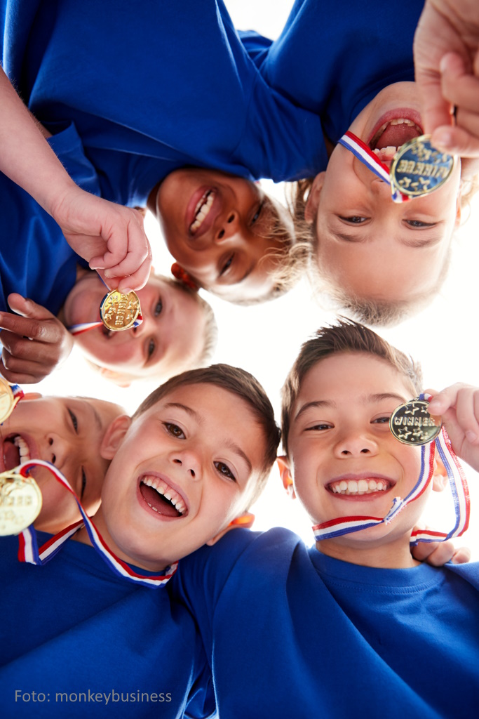 Im Kreis stehende Kinder mit Medaillen von unten fotografiert.(Froschperspektive)