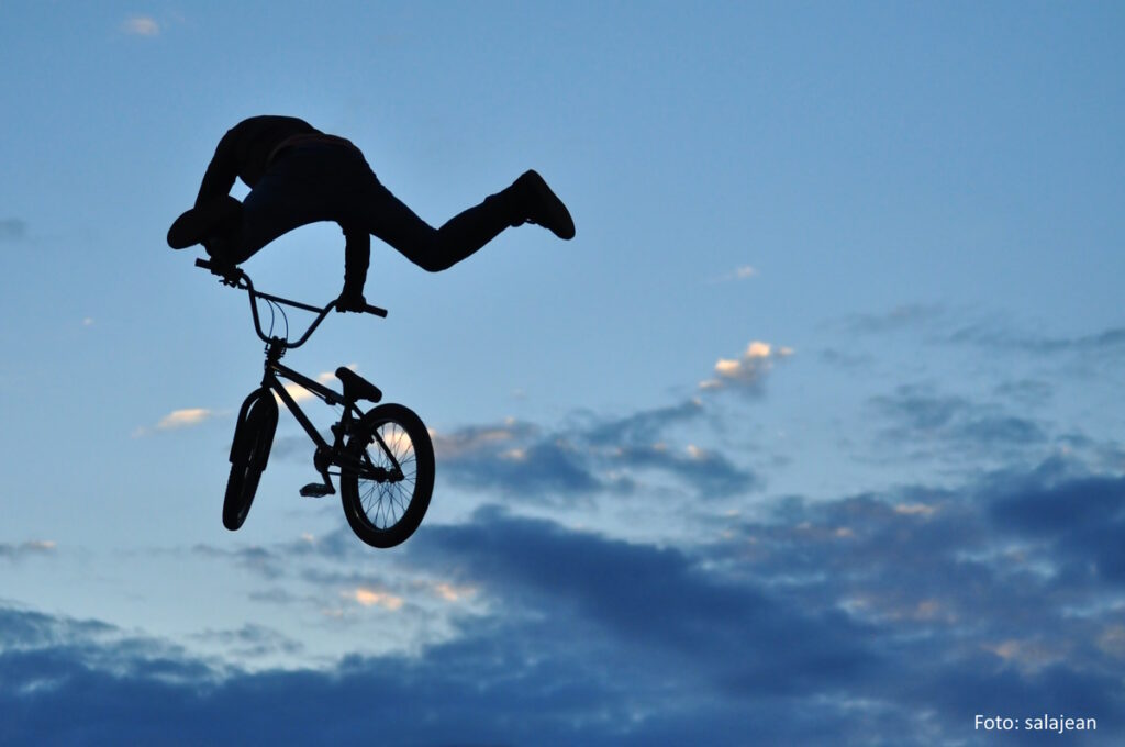 BMX-Fahrer:in springt vor dämmerndem Himmel in luftiger Höhe