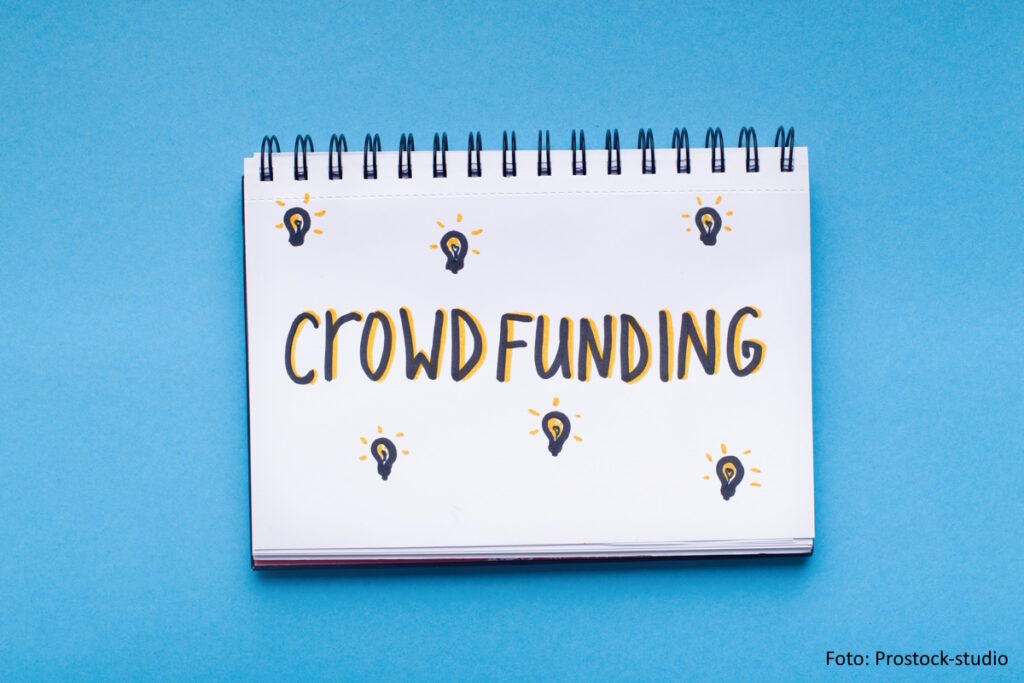 Schriftzug "Crowdfunding" auf einem weißen Ringblock vor hellblauem Hintergrund