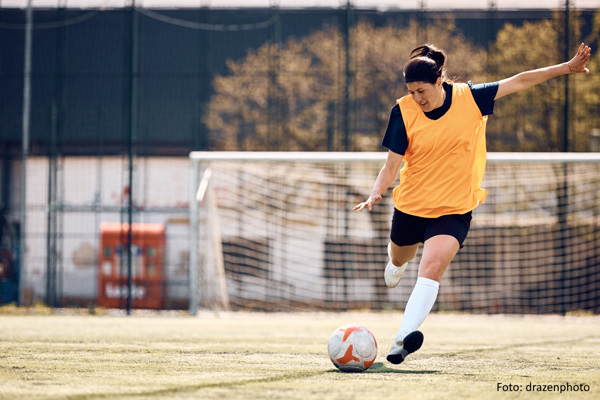 Female soccer player kicking the ball on playing field.