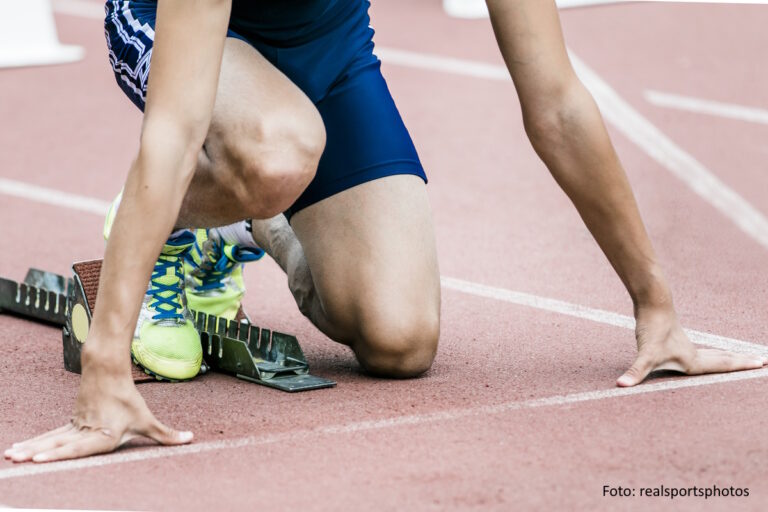 Männlicher Sprinter macht sich am Startblock bereit für den Lauf.