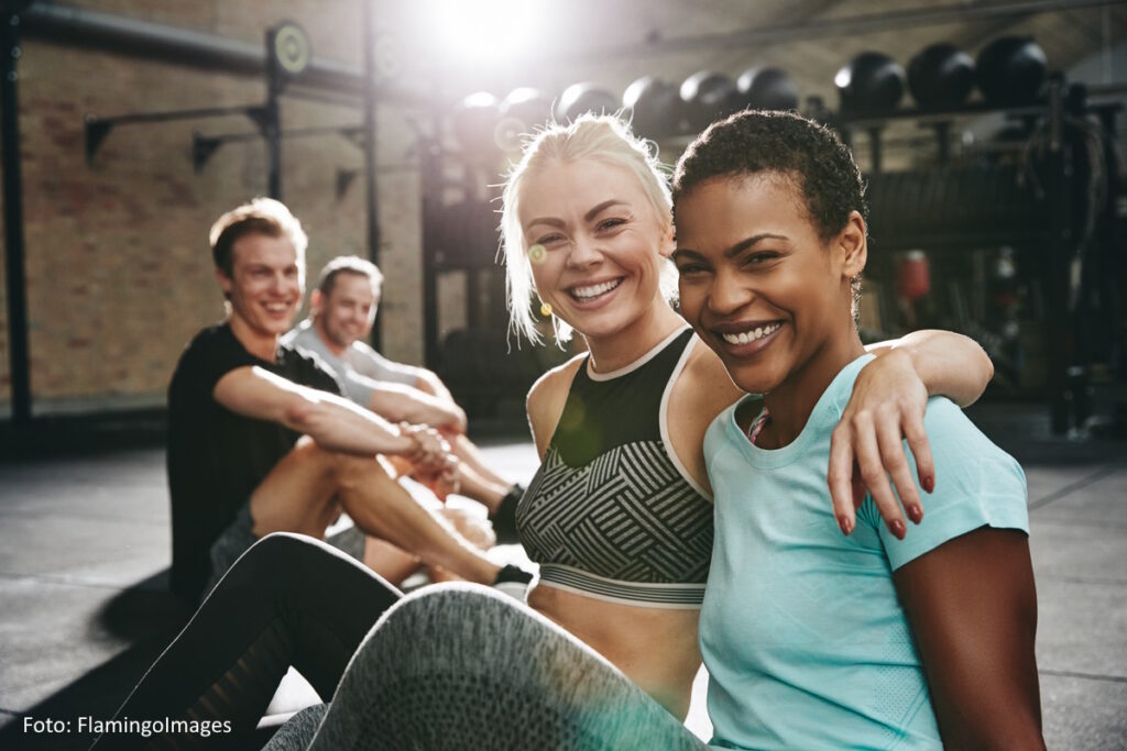 Vier Frauen und Männer sitzen in einem Fitnessstudio nach dem Training.