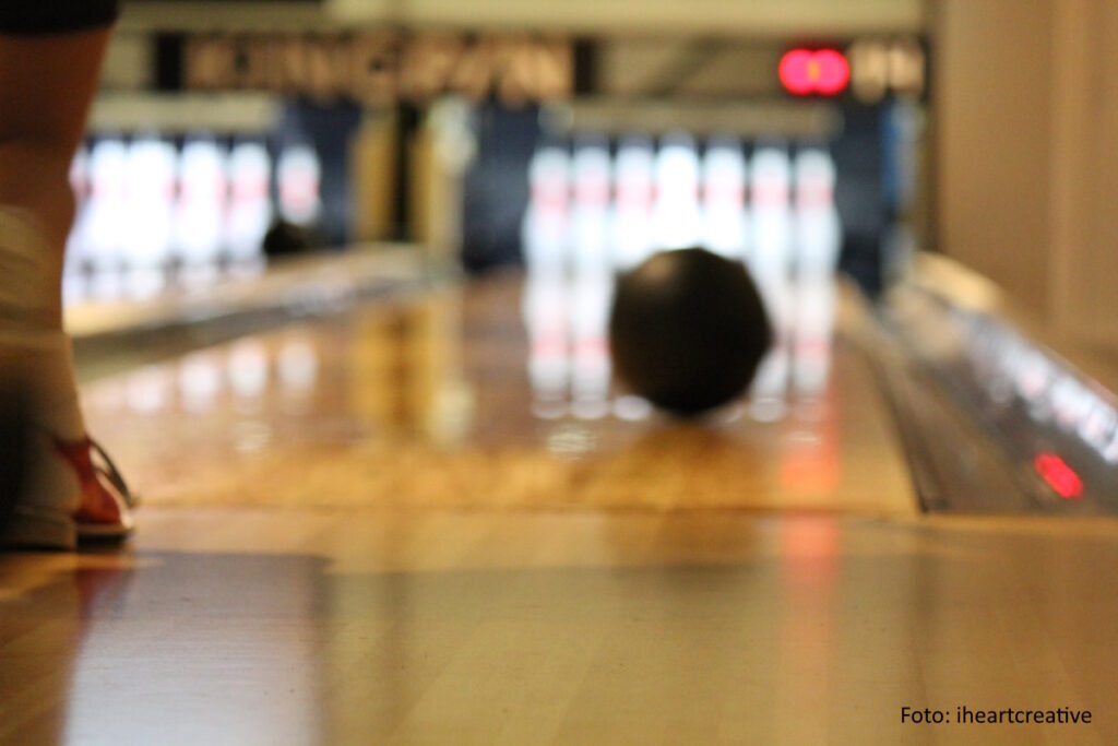 Bowlingball rollt auf einer Bowlingbahn den im Hintergrund stehenden Pins entgegen
