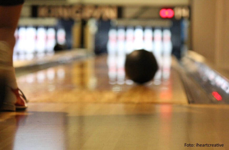 Bowlingball rollt auf einer Bowlingbahn den im Hintergrund stehenden Pins entgegen