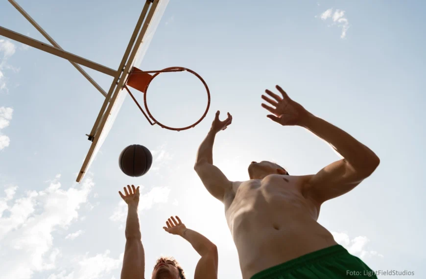 Aus der Froschperspektive: Zwei oberkörperfreie Männer beim Basketballspielen im Freien. Im Hintergrund: sonniger Himmel