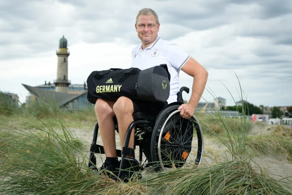 Para Athlet Marcus Klemp steht auf einer Düne vor dem Warnemünder Leuchtturm