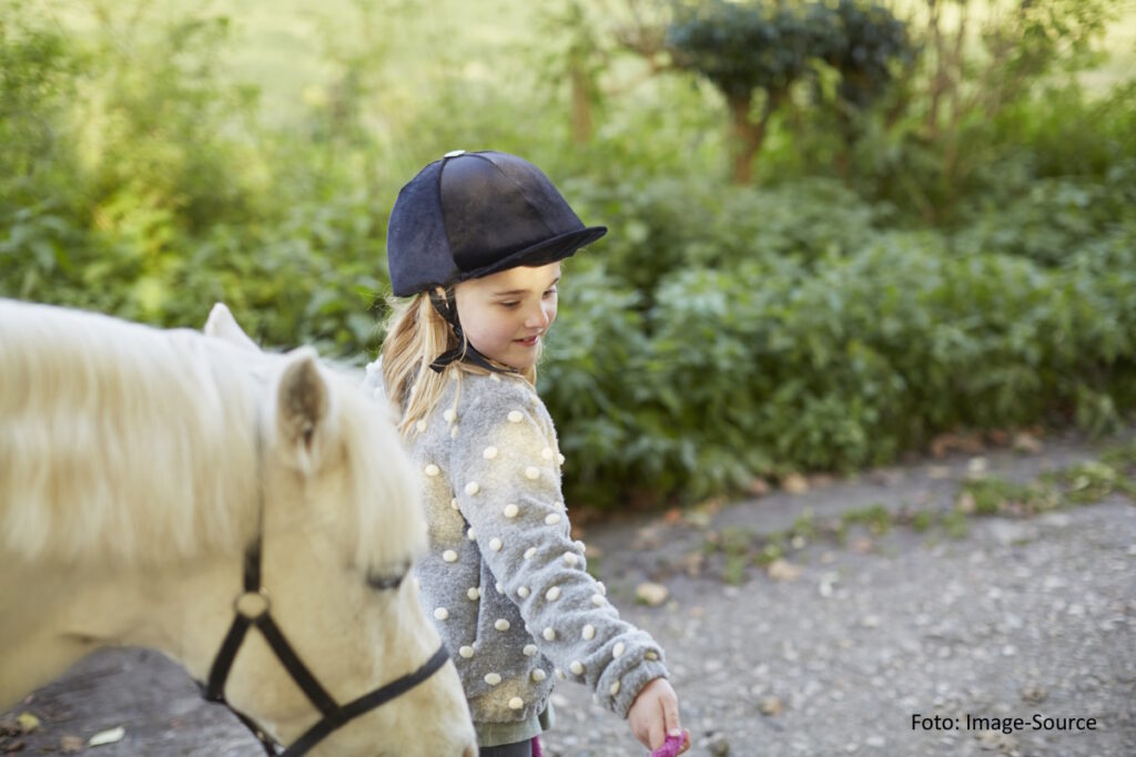 Mädchen mit Reiterhelm führt ein helles Pony am Zügel