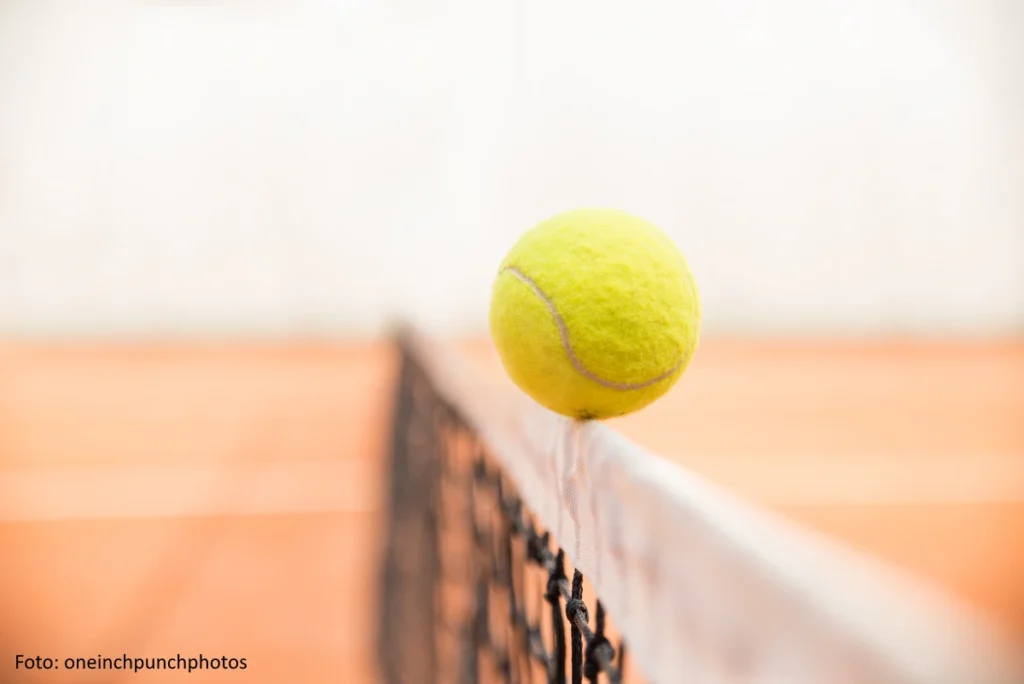 Ein Tennisball balanciert auf der Netzkante