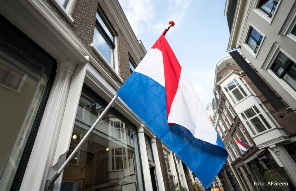 Eine niederländische Flagge weht in einer Häusergasse neben einem Schaufenster.