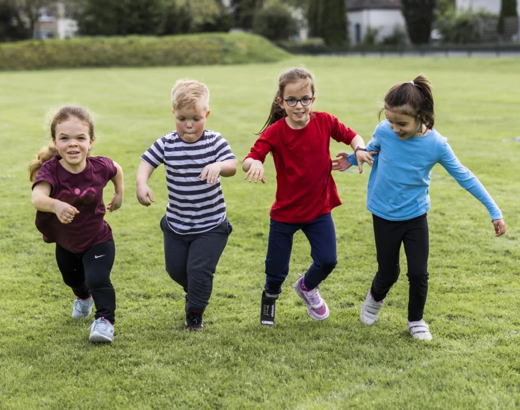 4 Kinder mit unterschiedlichen Behinderungen laufen über eine sommerliche Wiese.