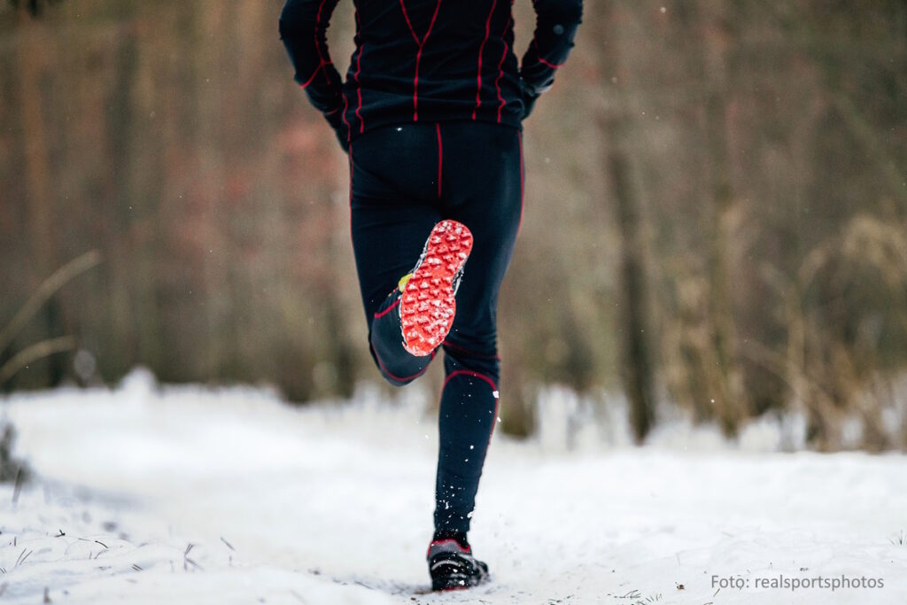 Laufsportler in langer, schwarzer Funktionskleidung läuft über einen schneebedeckten Waldweg.