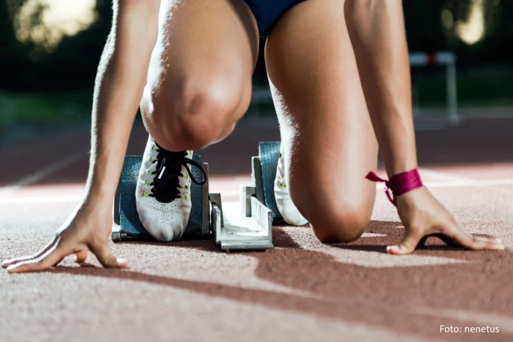 Junge Sprinterin im Startblock - zu sehen sind Beine und Arme der Athletin