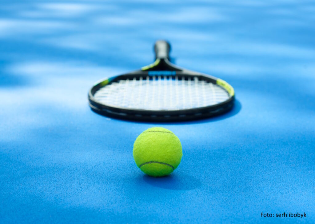 Yellow tennis ball is laying near professional racket on blue cort carpet. Made for playing tennis. Contrast image with satureted colors and shadows. Concept of sport equipment photo.