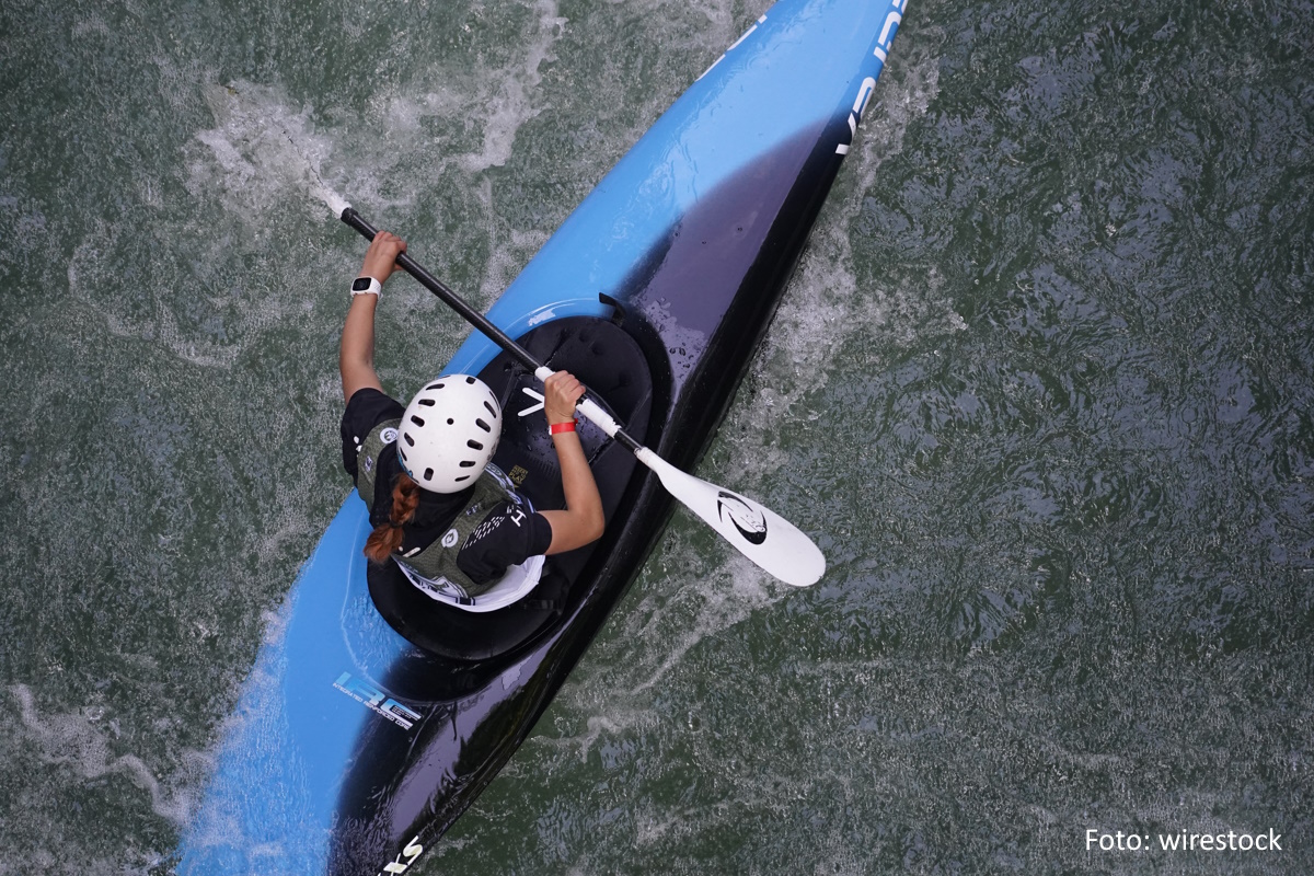 Draufsicht auf eine Kanusportlerin mit weißem Helm und in blauem Boot.