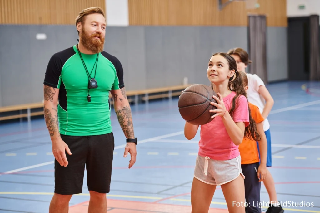 An den Armen tätowierter Basketballtrainer bringt Kindern den Freiwurf bei.