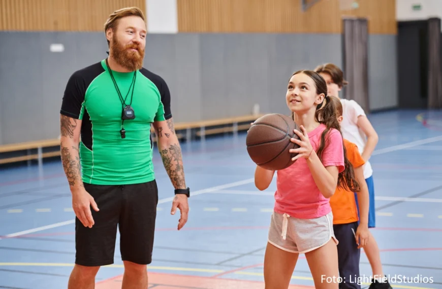 An den Armen tätowierter Basketballtrainer bringt Kindern den Freiwurf bei.