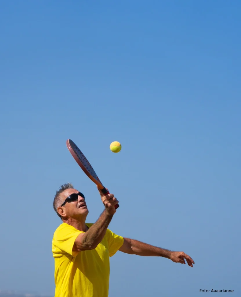Älterer Mann in gelbem Shirt spielt Beachtennis