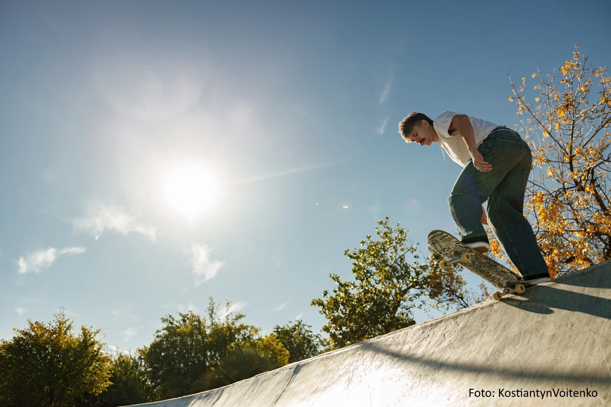 Skateboarder steht bei strahlendem Sonnenschein auf der Kante einer Halfpipe.