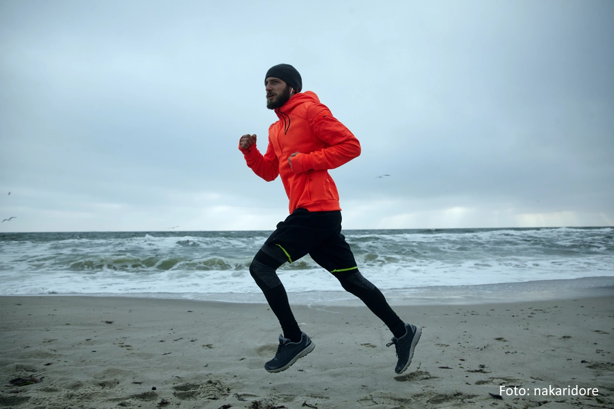 LĂ€ufer mit wetterfester Kleidung (orange Jacke, schwarze Hose) am Sandstrand