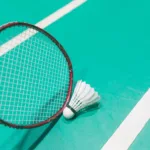 Badmintonschläger und Federball vor grünem Wettkampfcourt